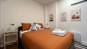 Moderni hotellihuone, jossa on suuri sänky, yöpöytä, patteri ja taideteoksia seinillä.