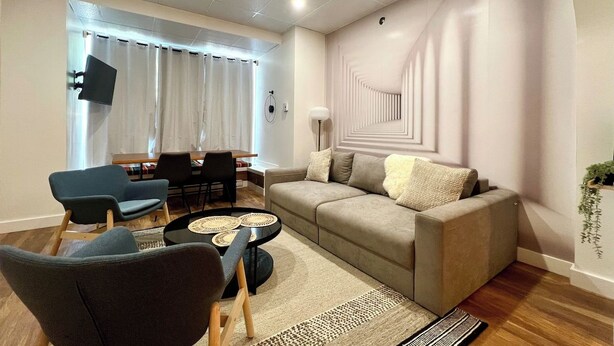 A modern living room with a sofa, armchairs, a coffee table, and a dining area with a table and chairs. - Stunning apartment in Saint-Roch (Québec)