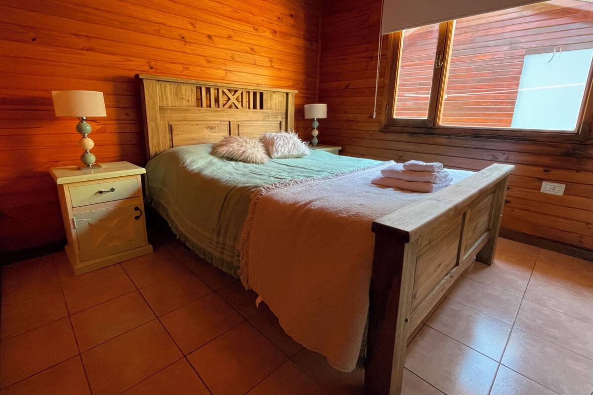 Quarto com painéis de madeira, uma cama, mesas de cabeceira e uma janela.