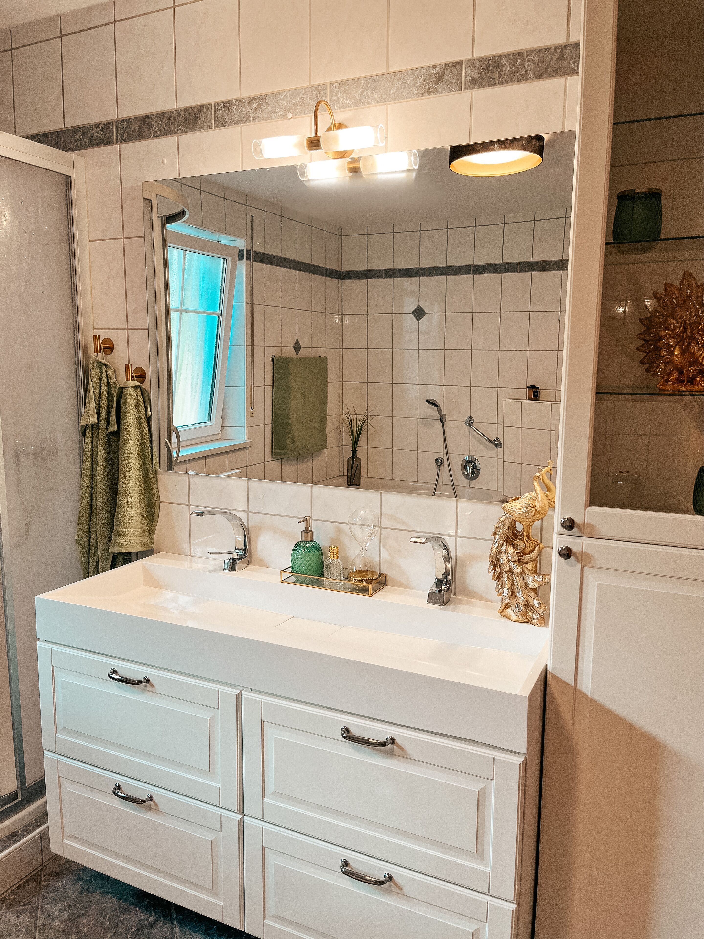 Un baño con tocador blanco, espejo, ventana y ducha.