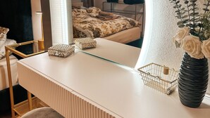 A modern hotel room with a white vanity, a round mirror, a vase with white flowers, and a bed with floral bedding. - Panorama retreat; incl. private whirlpool (Bad Kötzting)