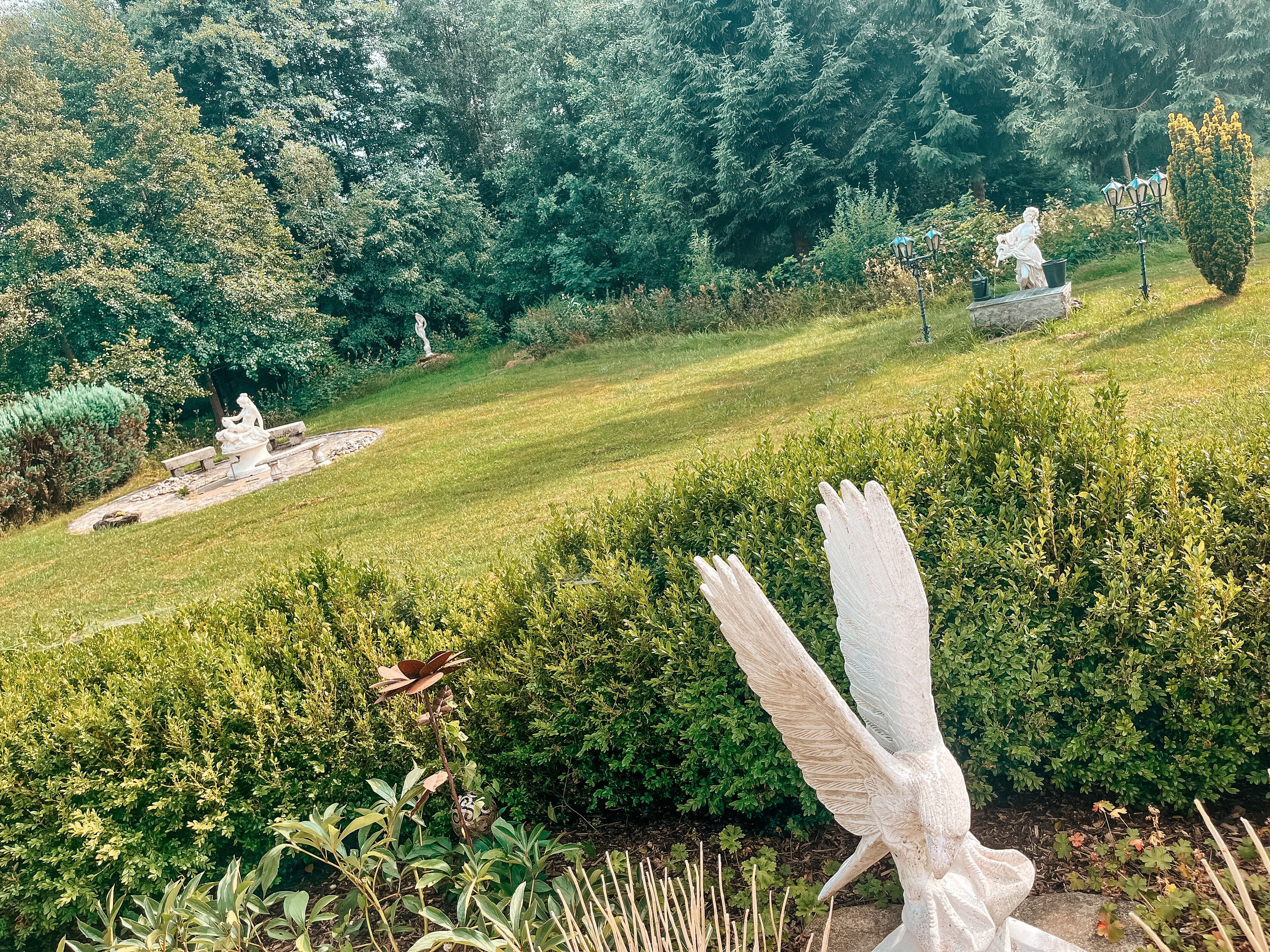 Ein Garten mit Statuen, einer Bank und vielfältigen Pflanzen.