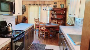 A compact kitchen with a stove, microwave, and sink. There is a dining table with chairs and a small shelf with kitchenware. - Rustic Lakeview Lodge at Bass Lake. Bookable boat slip! (Bass Lake)