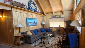 A cozy living room with a wooden ceiling, a large clock, a sofa with blue cushions, a coffee table, and a statue. - Rustic Lakeview Lodge at Bass Lake. Bookable boat slip! (Bass Lake)