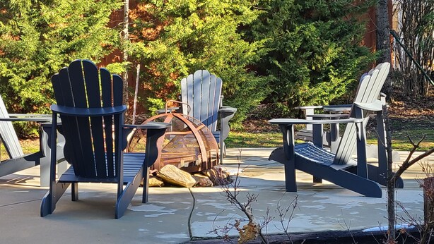 An outdoor seating area with Adirondack chairs and a table, surrounded by trees and a wooden barrel. - Rustic Lakeview Lodge at Bass Lake. Bookable boat slip! (Bass Lake)