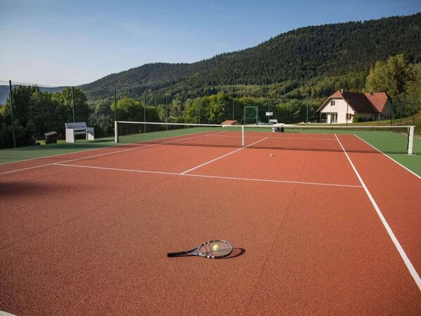 Una cancha de tenis con una red, una raqueta y una pelota en el suelo.
