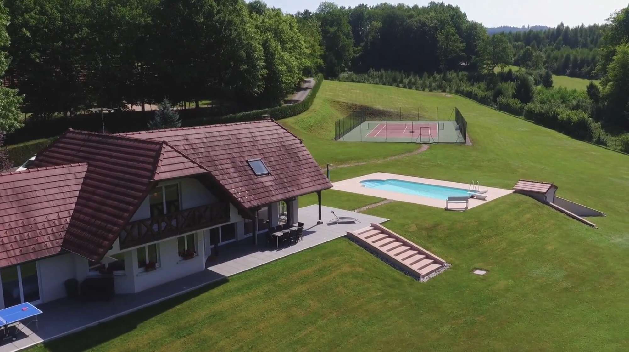 Ein Haus mit großem Garten, einem Swimmingpool und einem Tennisplatz.