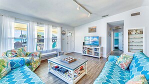 A living room with a large window, a television, and a bookshelf. - Beach Shack - Across Street From Beach, Private Swimming Pool, Pet Friendly! (St. George Island)