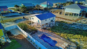 A coastal property with a large house on stilts, a swimming pool, and a view of the ocean. - Beach Shack - Across Street From Beach, Private Swimming Pool, Pet Friendly! (St. George Island)