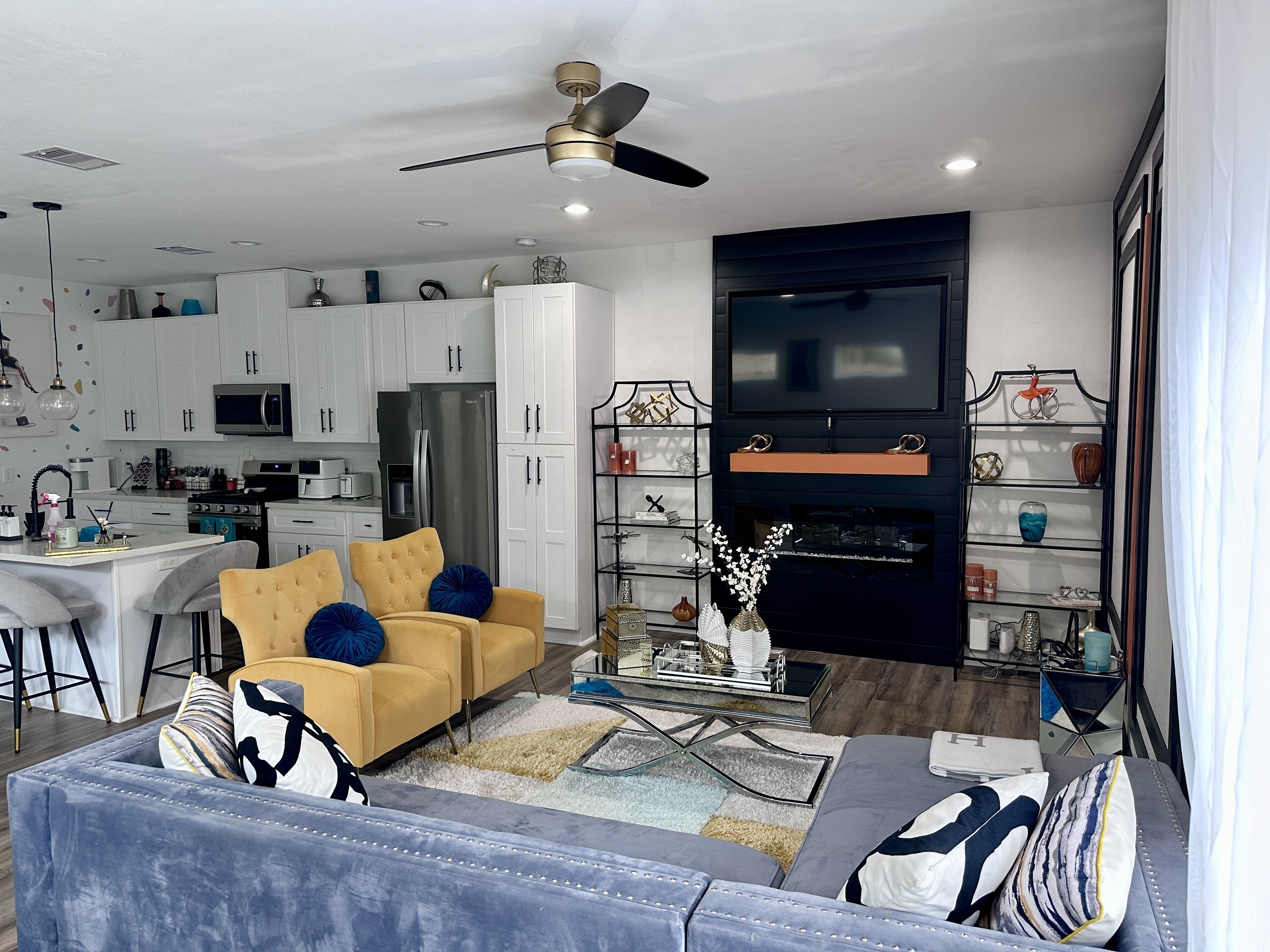 A modern living room with a sofa, coffee table, and TV. There is a kitchen area with cabinets and appliances.