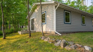 A cabin with a porch, surrounded by trees and a grassy yard.