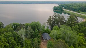A small cabin surrounded by dense forest, with a large body of water in the background.
