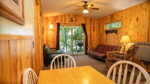 A cozy room with wooden walls, a ceiling fan, a sofa, a dining table, and chairs.