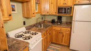 A kitchen with wooden cabinets, a white stove, a sink, a microwave, and a refrigerator.