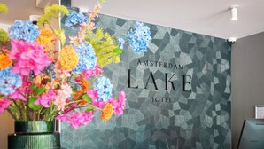 A reception area with a geometric patterned wall, a floral arrangement, and a Samsung monitor. - Amsterdam Lake Hotel  (Badhoevedorp)