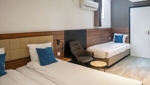 A hotel room with two beds, a chair, a small round table, and an air conditioning unit. - Amsterdam Lake Hotel  (Badhoevedorp)