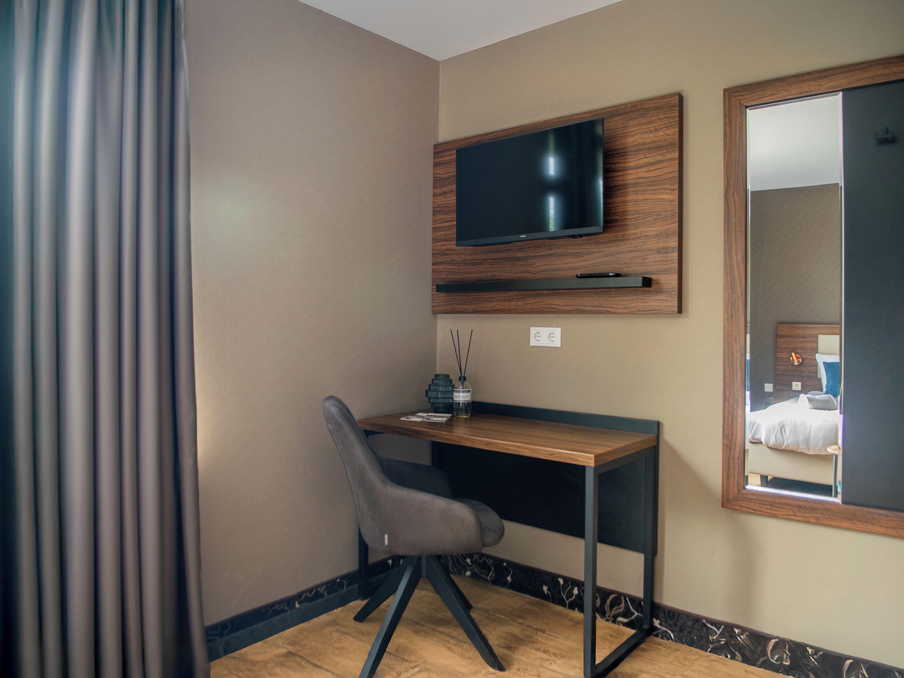Quarto de hotel com escrivaninha, cadeira, televisão e espelho.