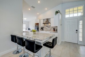 A modern kitchen with a large island, bar stools, and a white door. - ⚓Turtle Bay Cottage! Cozy home w/private pool! Water view!⚓ (Bradenton)