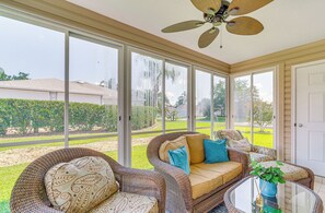A sunroom with wicker furniture, large windows, and a ceiling fan. - Charming Designer Home Near Lake Sumter (The Villages)
