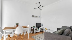 Ein modernes Wohnzimmer mit einem Holzesstisch, weißen Stühlen, einem grauen Sofa und einem Fernseher auf einer weißen Unterhaltungseinheit.
