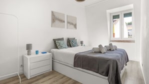 Ein Schlafzimmer mit Bett, Nachttisch, Lampe und einem Fenster.