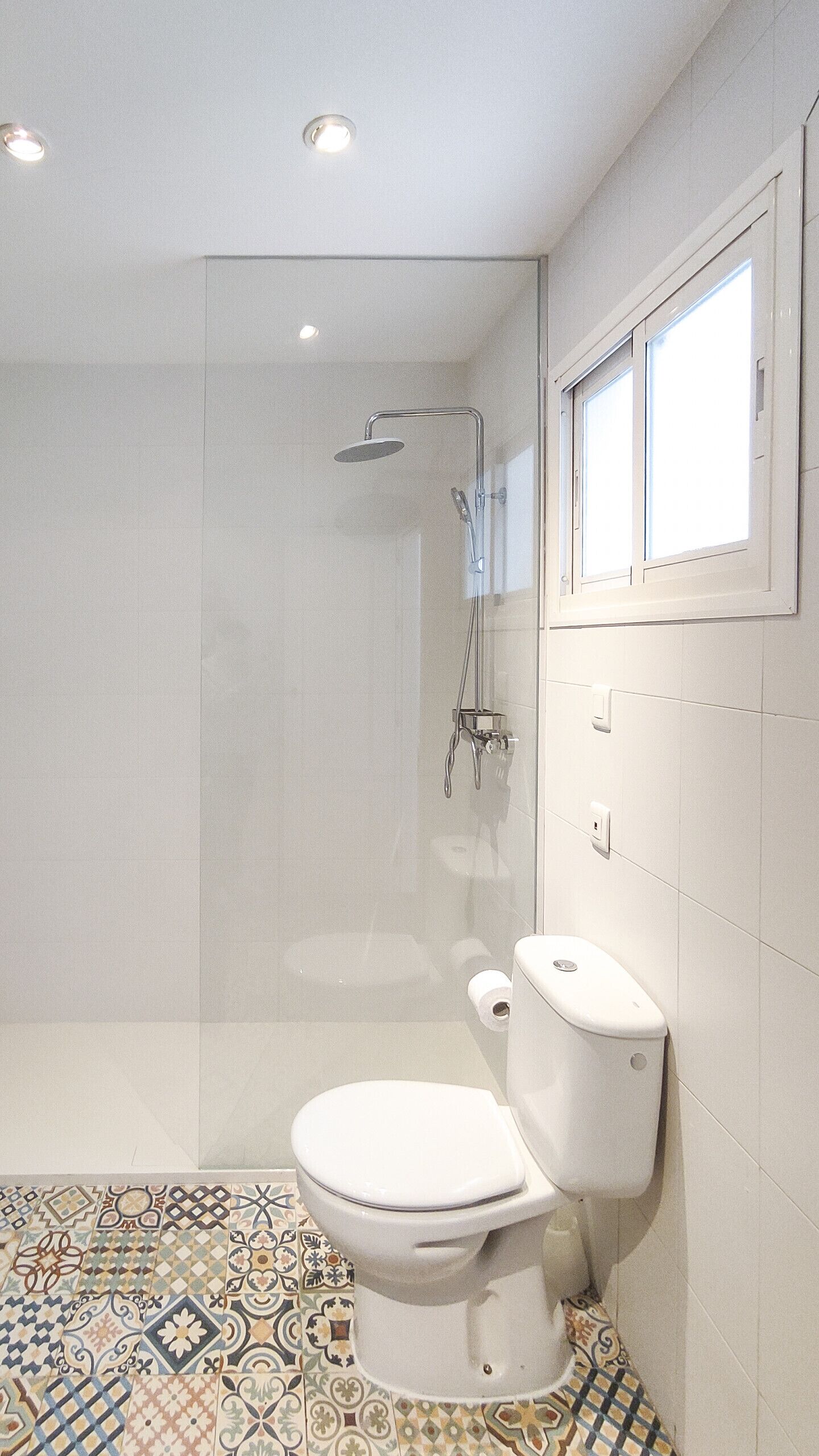 Een badkamer met douche, toilet en vloertegels met een patroon.