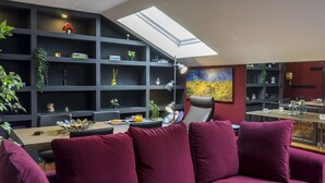 A modern living room with a dark wood table, a purple sofa, and a skylight above a shelving unit with plants and books. - Housing San Lorenzo by Sharing Co (Málaga)