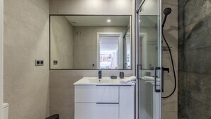 Un baño moderno con cabina de ducha de vidrio, un espejo grande y un tocador blanco con lavamanos y toallero.