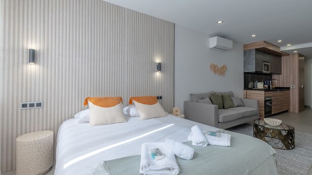 Una habitación de hotel moderna con una cama grande, un sofá, una pequeña mesa redonda y una kitchenette.