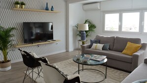 En moderne stue med et fladskærms-tv, en grå sofa med gule puder, et glas sofabord og en sort-hvid lænestol.