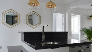 Et moderne køkken med en sort bordplade, spejle med gyldne rammer og hængende lamper.