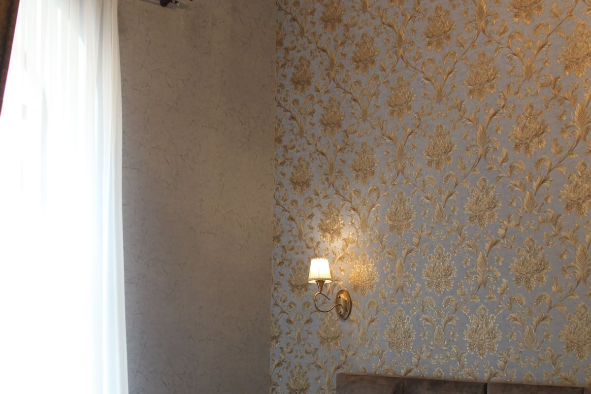 A neatly made bed with a headboard, a nightstand with a lamp, and a window with curtains.