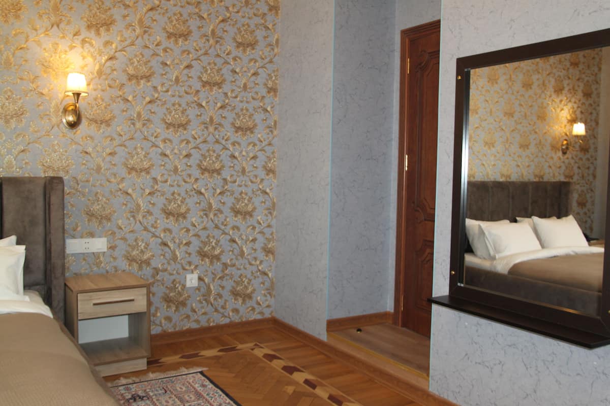 A bedroom with a bed, nightstand, mirror, and patterned wallpaper.