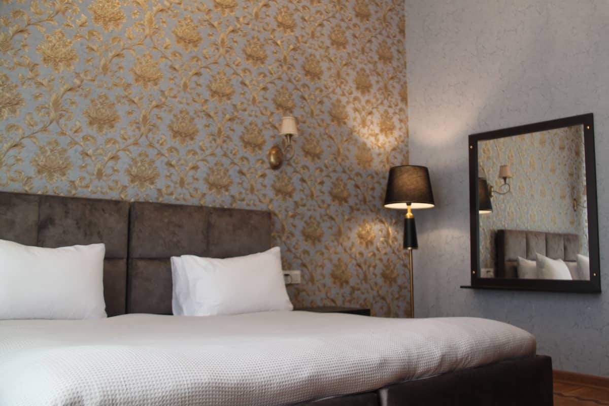 A hotel room with a large bed, a headboard, a wall-mounted lamp, and a mirror.