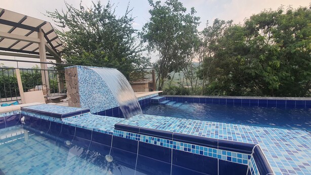 A swimming pool with a waterfall feature, surrounded by trees and a covered area. - Vista Hermosa Glamping & Cabañas (La Mesa)