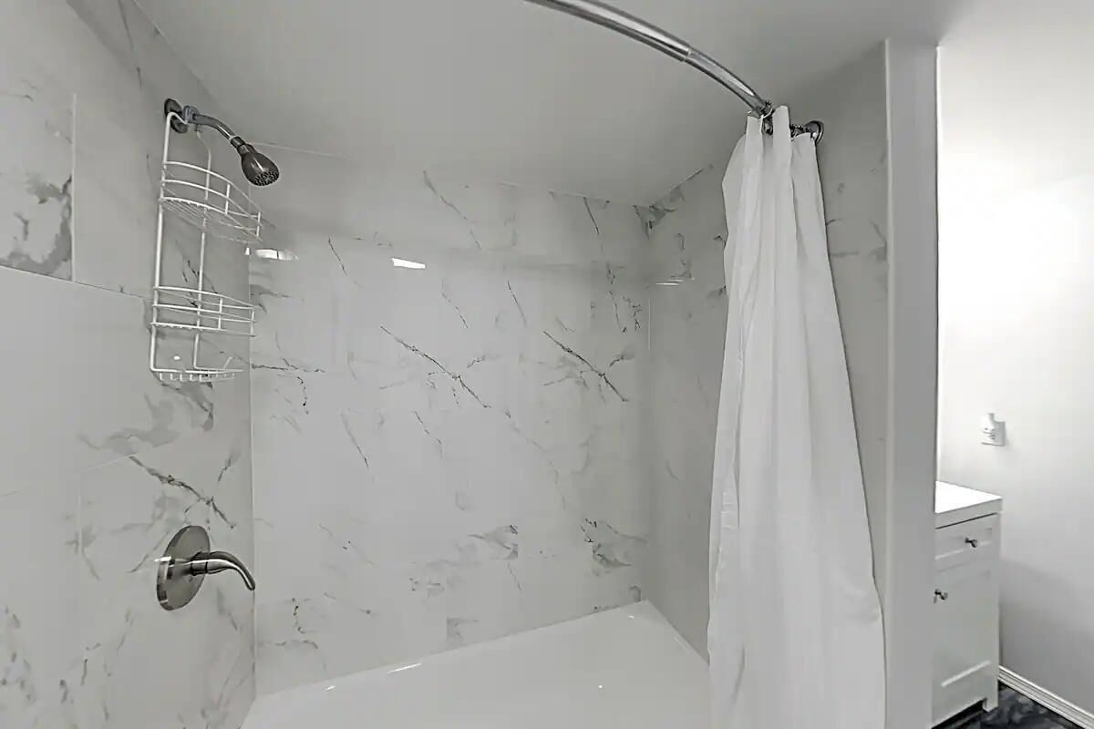 Une salle de bain moderne avec une douche, un mur en marbre blanc et un petit meuble blanc.