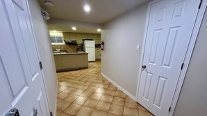 A hallway with a kitchen area in the background, featuring a tiled floor and white doors. - Short Walk to the Falls,SuperLargeApt,Free parking (Niagara Falls)