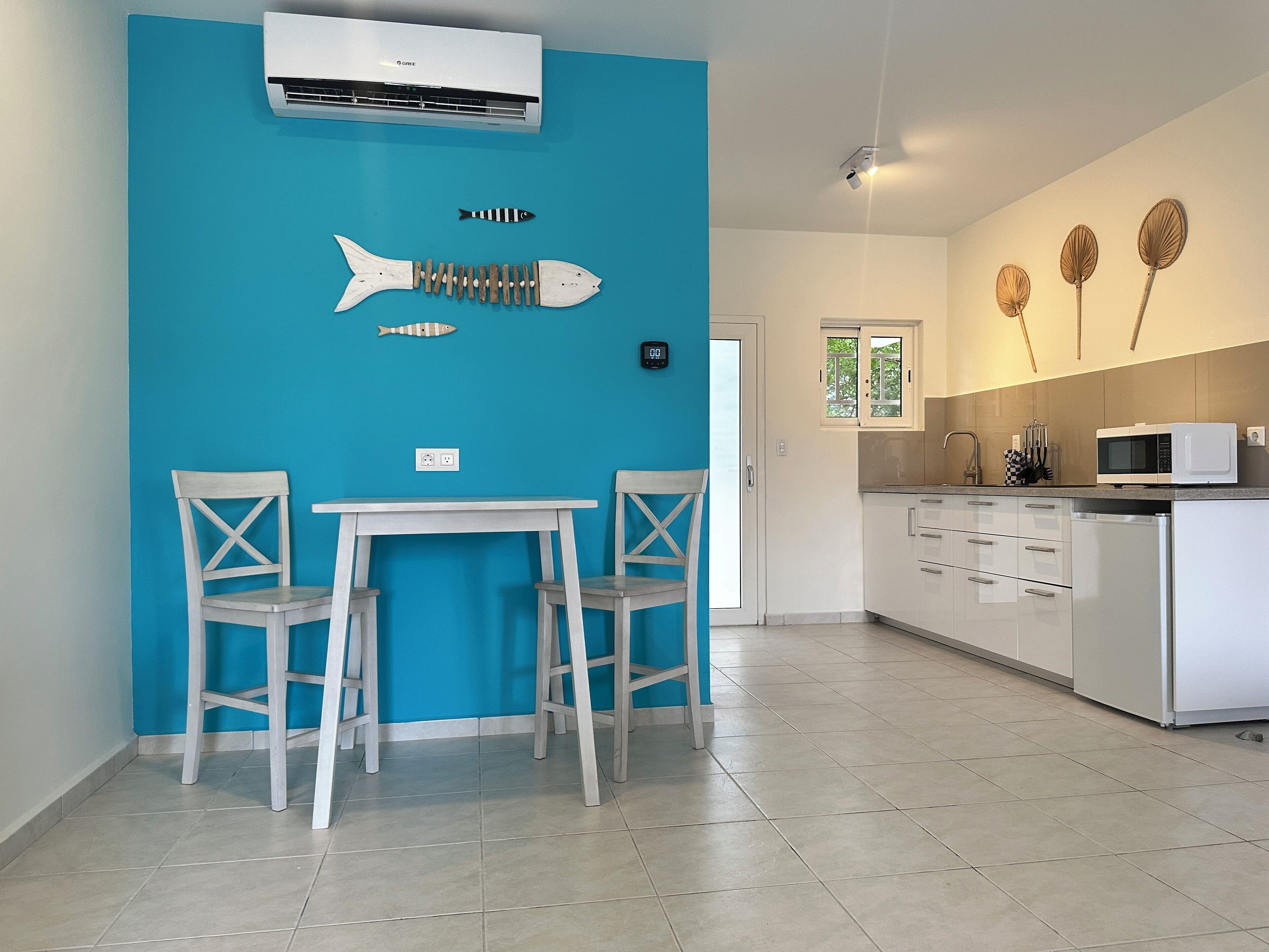 Una cocina moderna con armarios blancos, un microondas y un lavamanos. Hay una zona de comedor con una mesa y dos sillas.