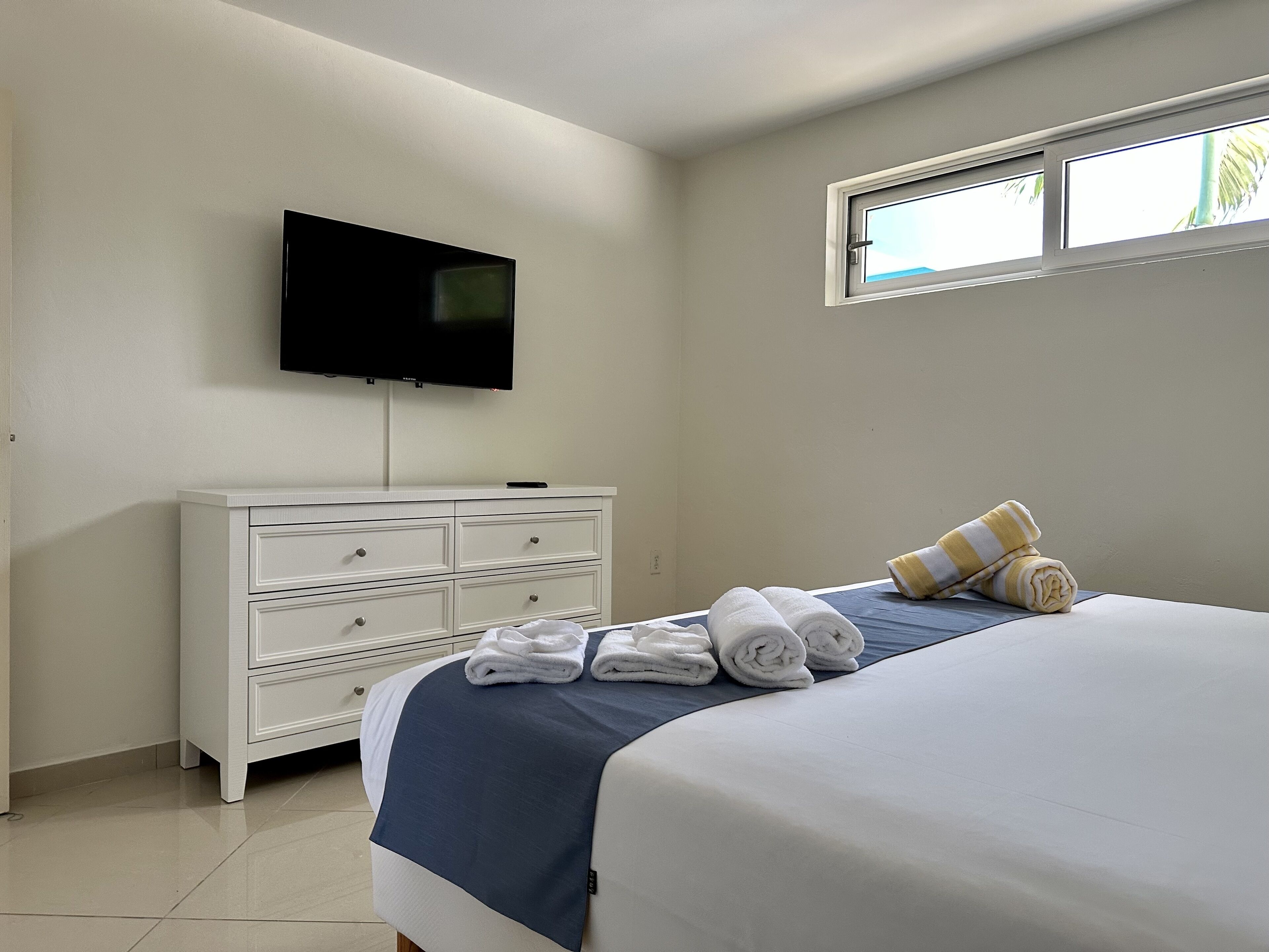 A bedroom with a bed, a dresser, a television, and a window.