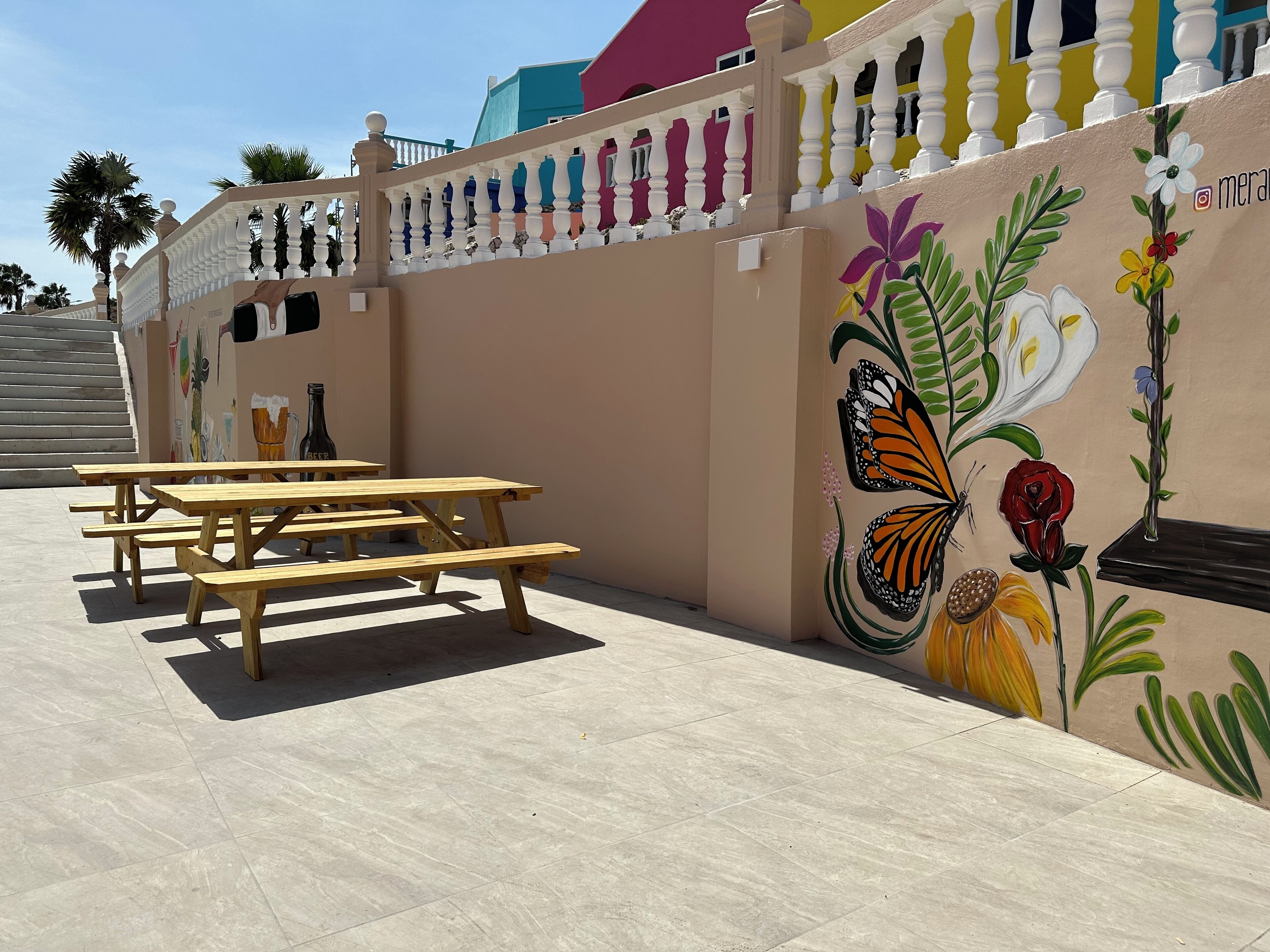 A patio area with wooden picnic tables and a mural of butterflies and flowers on the wall.