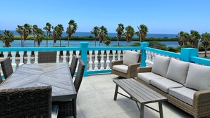 A terrace with wicker furniture, a view of the ocean, and a turquoise railing. - MERAKII SEAVIEW ESCAPE CURACAO (Willemstad)