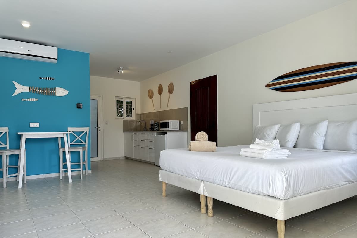 A hotel room with a bed, a small kitchenette, a dining table with chairs, and a blue accent wall.