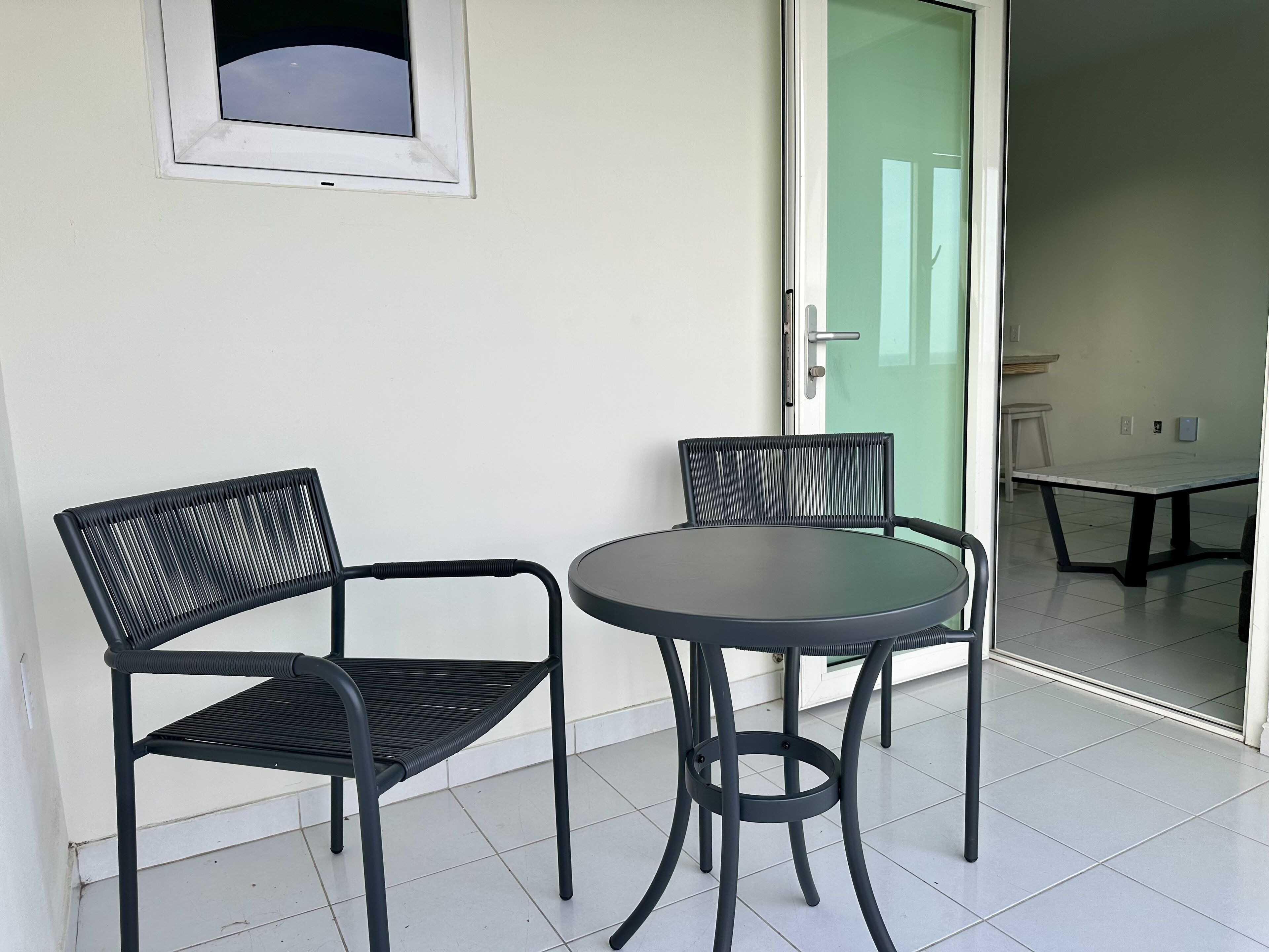 Een balkon met twee zwarte metalen stoelen en een klein, rond tafeltje.