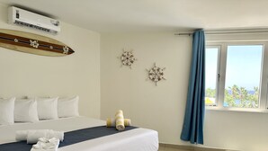 A hotel room with a bed, a wall-mounted air conditioner, decorative wall art, and a window with a view of palm trees. - MERAKII SEAVIEW ESCAPE CURACAO (Willemstad)