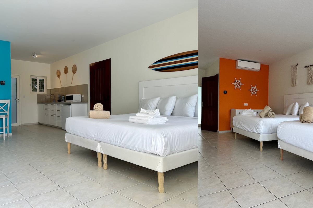 A hotel room with two beds, a kitchenette, and a bathroom.