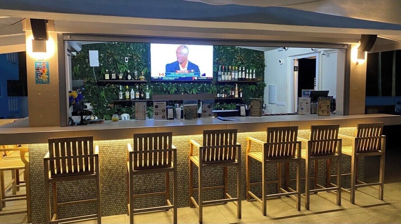 Eine Bar mit Fernseher, Barhocker und Regalen voller Flaschen.