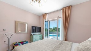 A bedroom with a large bed, a television on a dresser, a colorful bench, and a balcony with a pool. - Holiday Home Endi - rural escape with pool (Danilo Kraljice)