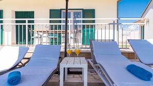 A sunlit outdoor seating area with lounge chairs and a table, featuring a view of a building with green shutters. - Holiday Home Endi - rural escape with pool (Danilo Kraljice)