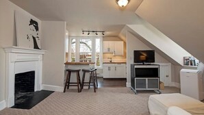 Ett kompakt bostadsutrymme med en öppen spis, en matplats, ett litet kök och en TV.