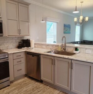 A kitchen with light-colored cabinets, a stainless steel sink, a dishwasher, and a marble countertop. - New! Oceanview Oasis whole house - Theater - Screened Porch - Sundeck - Grill (Marathon)